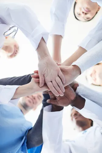 Directly,Below,View,At,Multi-ethnic,Group,Of,Doctors,Stacking,Hands